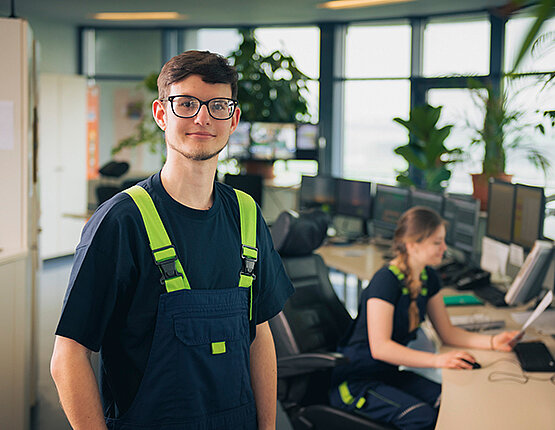 Junger Mann in Arbeitskleidung lächelt in die Kamera.